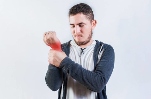 Suffering young man with pain in hand joints isolated. Person with arthritis pain rubbing hand
