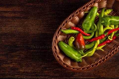 A brown basket with green and red peppers on a wooden base