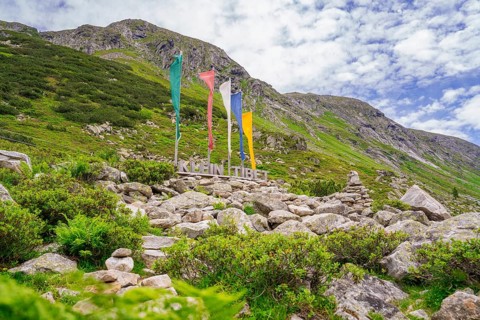 Landscape in the mountains with colourful flags, a sign and green vegetation, framed by rocks,