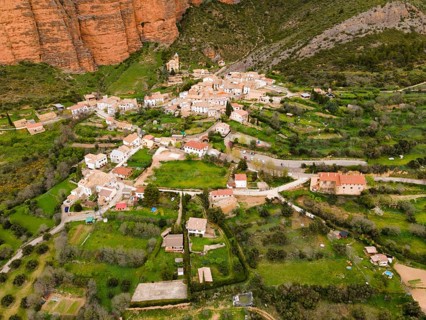 Aerial view of a picturesque village surrounded by green hills and striking orange rocks, aerial
