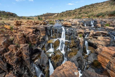 Waterfalls between orange-coloured rocks on the Treur River, Bourke's Luck Potholes, long exposure,