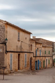 Medieval village street with stone buildings and colourful shutters under a cloudy sky, Sineu,