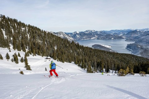 Skiers skiing down the Simetsberg, view of Walchensee and mountain panorama, Estergebirge, Bavarian