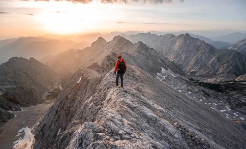 Mountaineer with helmet on a narrow rocky ridge at sunrise, crossing the Jubiläumsgrat, view of