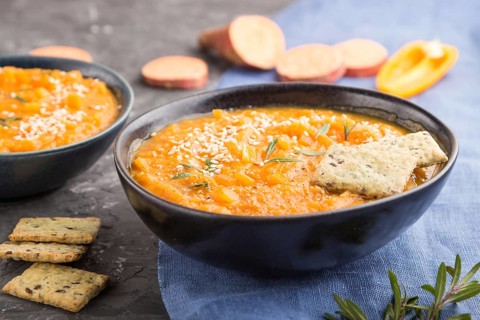 Sweet potato or batata cream soup with sesame seeds and snacks in blue ceramic bowls on a black