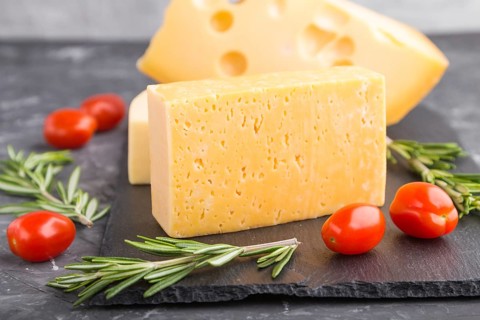 Various types of cheese with rosemary and tomatoes on black slate board on a black concrete