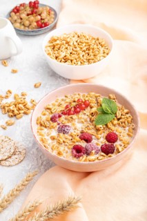 Wheat flakes porridge with milk, raspberry and currant in ceramic bowl on gray concrete background