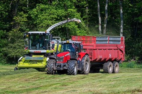 Tractor with trailer running beside Claas Jaguar 870 forage harvester, self-propelled silage