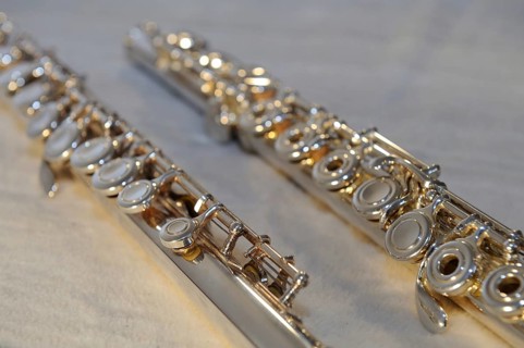 Close-up of two silver transverse flutes on a light-coloured surface