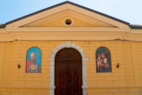 Yellow building with religious murals and large wooden door, radiates historical atmosphere,