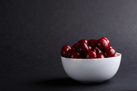 Fresh red sweet cherry in white bowl on black background. side view, copy space