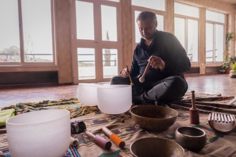 A mature Caucasian man performing with a quartz singing bowl amidst a collection of vibrational
