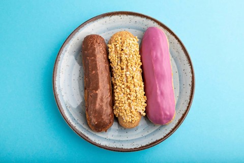 Set of eclair, traditional french dessert on ceramic plate on blue pastel background. top view,