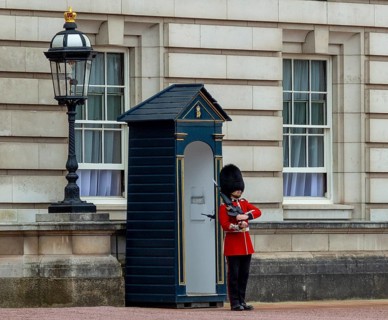 A guard in red uniform stands in front of a guardhouse next to a lantern at Buckingham Palace,