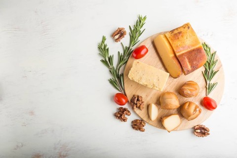 Smoked cheese and various types of cheese with rosemary and tomatoes on wooden board on a white