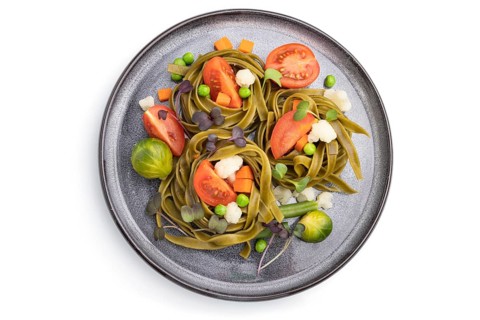 Tagliatelle green spinach pasta with tomato, pea and microgreen sprouts isolated on white