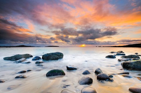 Orange coloured cloudy sky at sunset on a sandy beach strewn with round stones near Achiltibuie on