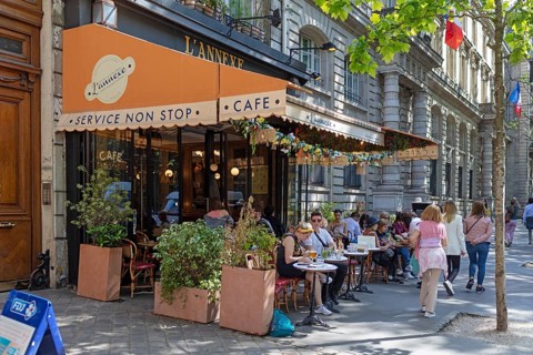 Street café with people sitting at tables, surrounded by plants and an awning, Paris
