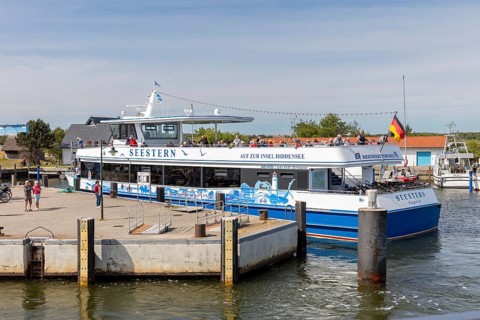 A large passenger ship with a flag is moored at the jetty in the sunny harbour, Rügen, Hiddensee