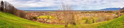 Panoramic view of a village with green meadows and trees, mountains in the background under a