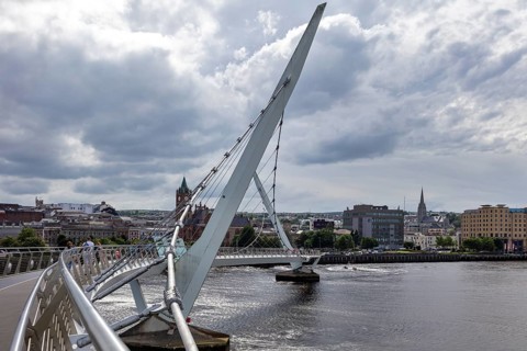 A deserted bridge over a tranquil river with dramatic clouds in the sky, Londonderry