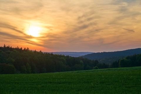 Sunset over a green meadow, surrounded by forest and hills under a cloudy sky, summer, Mönchberg,