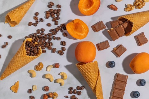 Ice cream cones with coffee beans, apricots, nuts and chocolate on a marble background