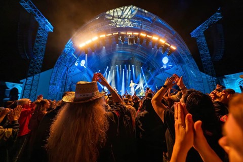 Concertgoers applaud at a night-time concert with blue lights on stage, Klostersommer, Calw Hirsau,