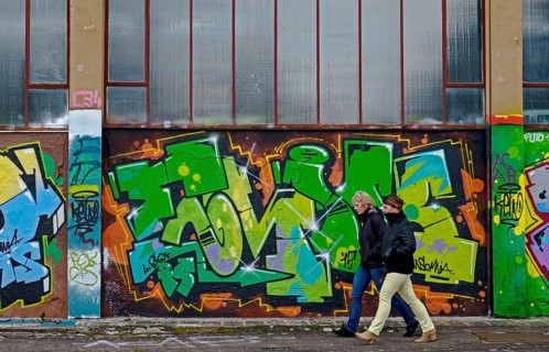 Two people walking along a wall covered with colourful graffiti, urban ambience, Landau,