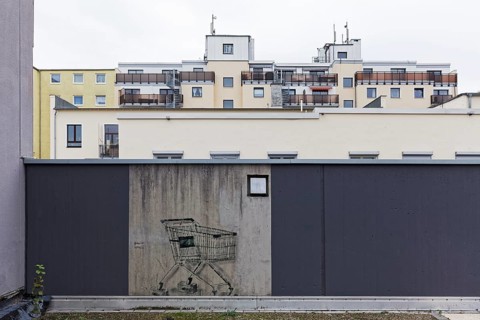 Shopping trolley with bricks instead of wheels, only preserved mural on a freshly painted wall,