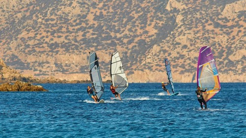 Windsurfers enjoy the sunny weather on the blue sea in front of a rocky coast, windsurfers, Meltemi