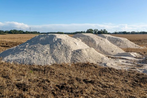 Piles of lime calcium carbonate in field for liming farmland soil, Suffolk, England, UK