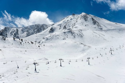 Schneebedeckte Berge unter blauem Himmel, mit Skiliften und einigen Skifahrern auf den Pisten,