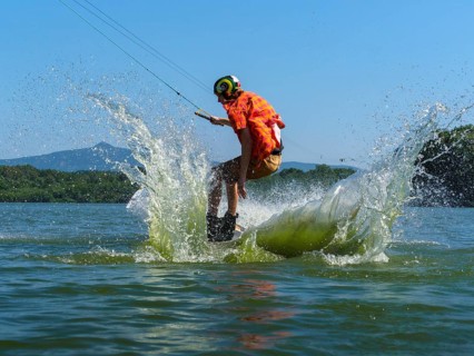 Young casual man with flapping shirt on wakeboard jumping into the lake, water ski and wakepark,
