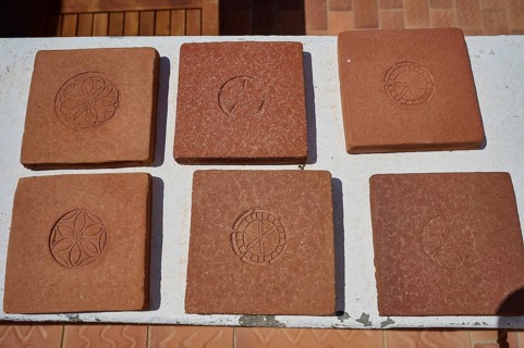 Six square clay bricks with different geometric and floral patterns laid on a white table top,