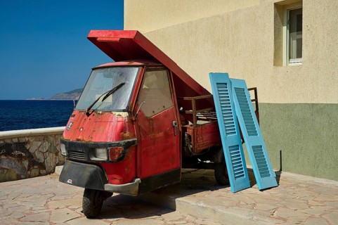 Weathered red tricycle next to blue shutters on the coast, Mandraki, Nisyros, Dodecanese, Greek
