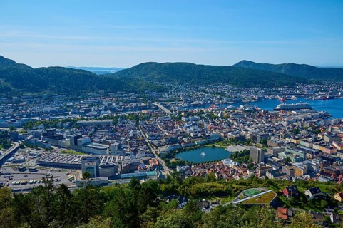 Panoramic view of a coastal town with harbour and a variety of buildings, surrounded by mountains