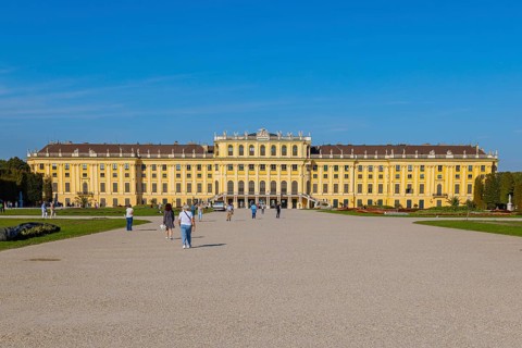 Schönbrunn Palace with yellow facade and blue sky in the background, some tourists in the