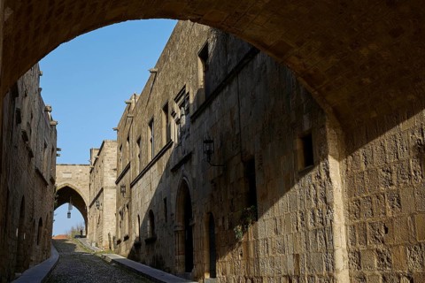 Stone path under an arch, surrounded by medieval, historic buildings with shade, Knights Street,