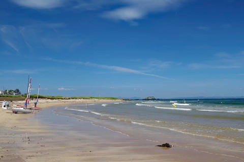 Quiet beach with boats on the shore and blue sky with scattered clouds, North Berwick, Scotland,