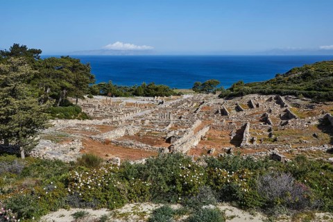Ruins of an ancient city overlooking the sea, surrounded by vegetation under a blue sky, Kamiros,