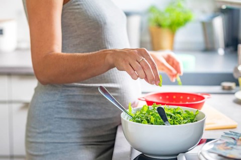 A pregnant woman prepares a healthy meal with fresh ingredients in the kitchen