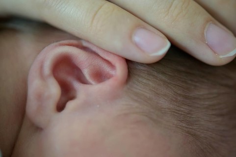 Close-up of a baby whose ear is gently touched by a hand