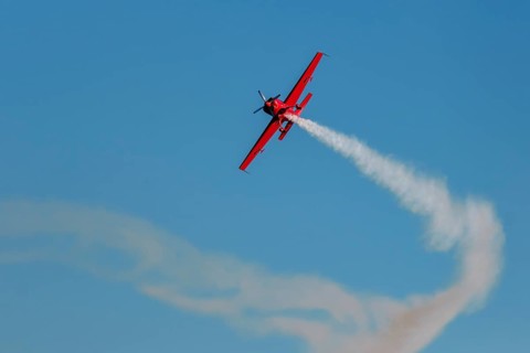 Red stunt aerobatic plane performing stunts in blue sky. Concept of speed, difficulty, precision,