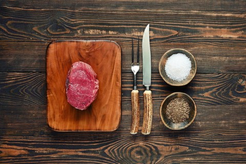 A fresh prime cut of beef steak on a chopping board, next to bowls of salt and pepper, with a