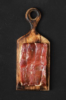 Juicy block of cured duck meat on a handcrafted wooden cutting board against a dark background