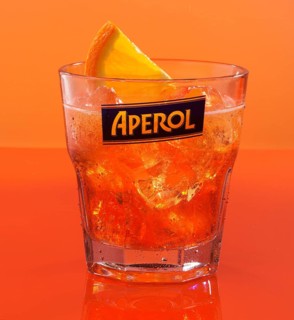 Aperol on ice cube cubes with half an orange slice in an aperitif tumbler against an orange