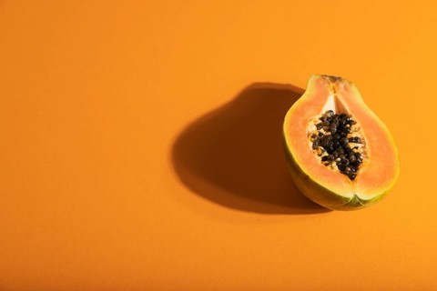 Ripe cut papaya on orange pastel background. Side view, copy space, hard light. Tropical, healthy
