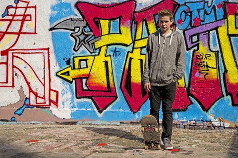 Thirteen-year-old boy with skateboard in front of graffiti, Cologne, Germany, Europe