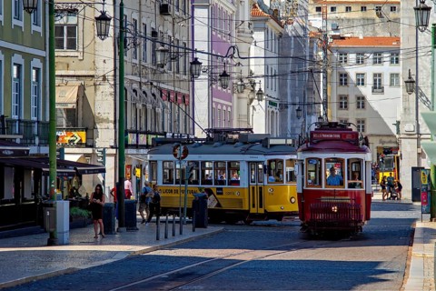 Historic trams navigate a bustling street in sunny Lisbon surrounded by classic architecture,